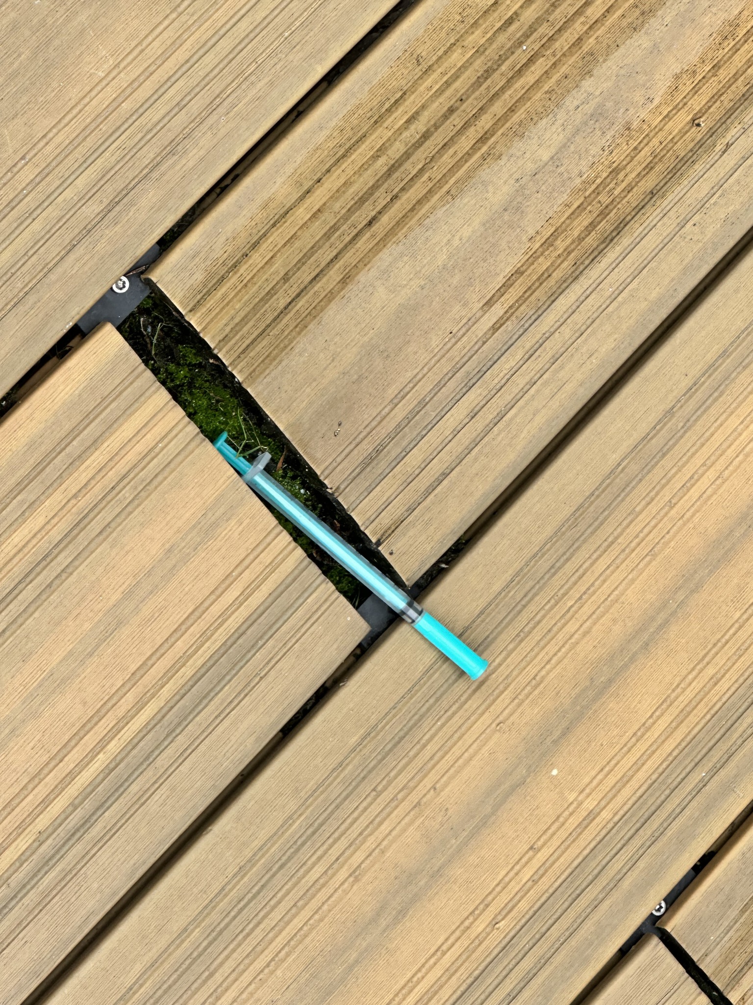 Discarded needle partly concealed between exterior decking boards at a commercial property in central Bristol